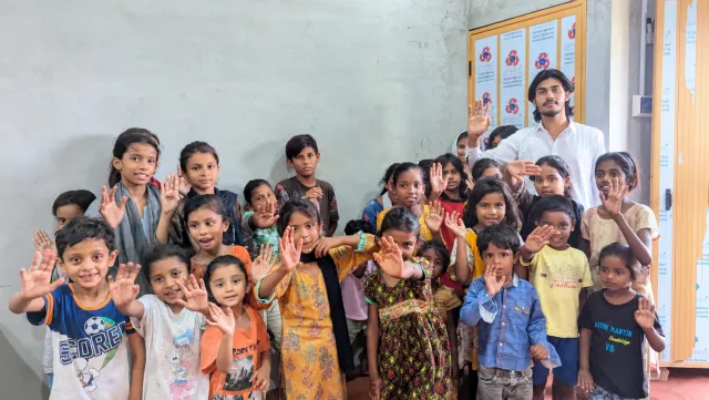 A group of smiling children waving inside a classroom