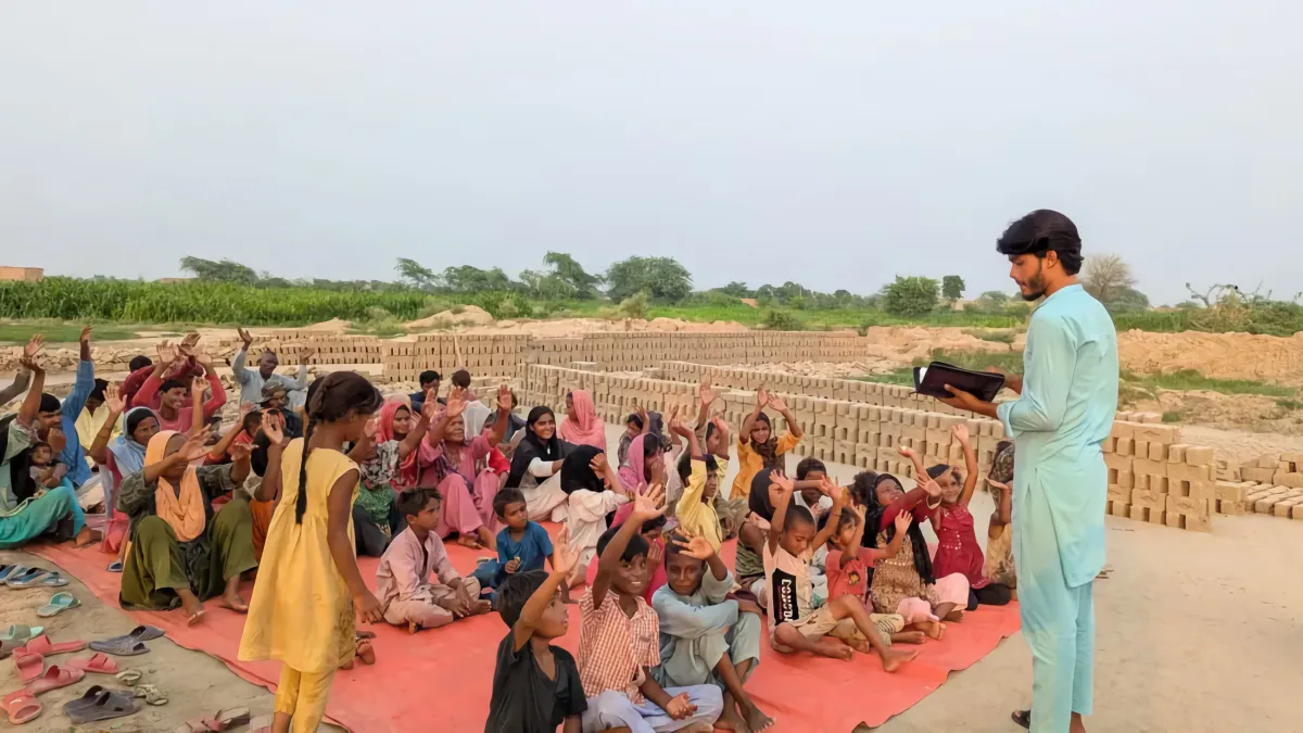 Children sitting outdoors during Sunday school, raising their hands to answer